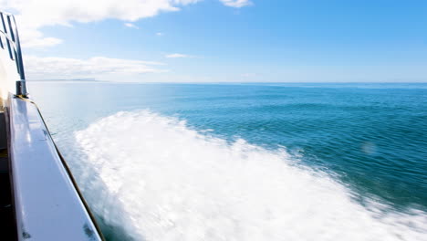 boat speeds out on blue open ocean, calm surface - forward facing shot over side