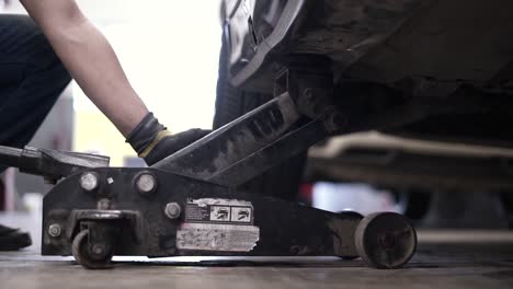 Slow-motion-shot-of-a-mechanic-jacking-up-a-car-in-a-garage