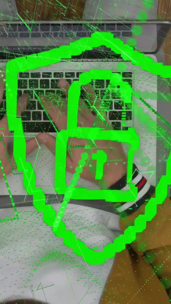 Video verticale: Uomo che tiene un dispositivo sopra un laptop alla scrivania, creando uno scudo tecnologico verde, e digita per accedere.
