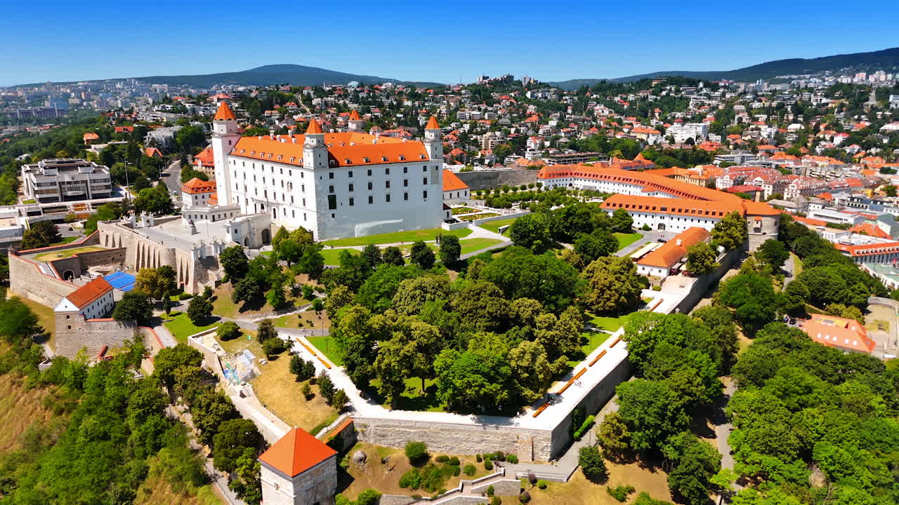 Frodigt grønt omgiver det smukke Bratislava Slot, der ligger på bakken. Luftperspektiv over den solrige byudsigt over den gamle bydel.