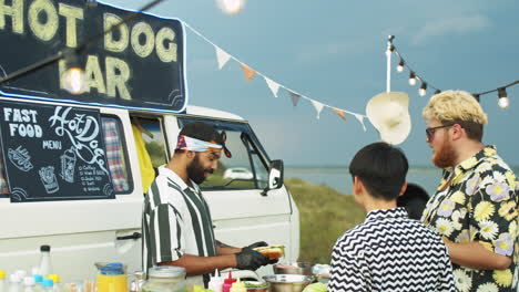 Hombre-Del-Medio-Oriente-Preparando-Perritos-Calientes-Para-Los-Clientes-En-El-Camión-De-Comida