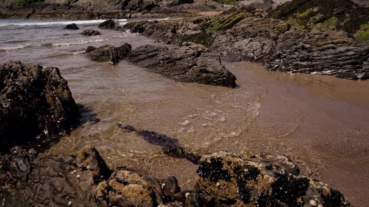 Onde oceaniche che si infrangono su una costa rocciosa e pozze di marea su una spiaggia sabbiosa in un ambiente costiero naturale