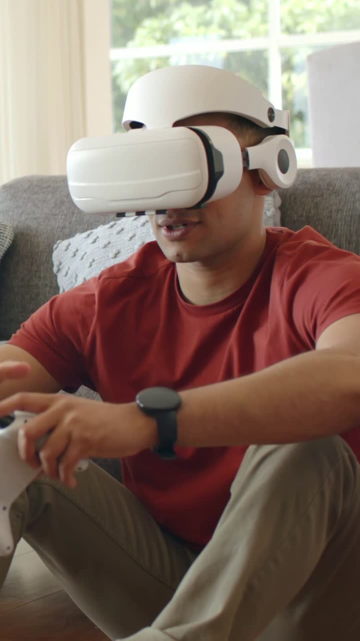 Video verticale: Uomo con una maglietta rossa che reagisce all'avvio di un'app VR, guidando con un controller bianco sul divano.