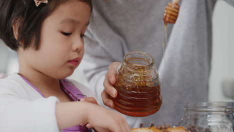 asian family having breakfast mother pouring honey on pancakes for little girl mom preparing homemade meal for daughter at home 4k