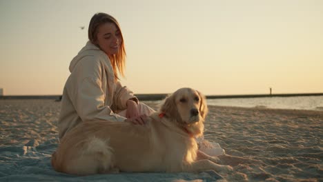 A-blonde-girl-sits-on-a-sunny-beach-with-her-dog-in-a-light-color-in-the-morning