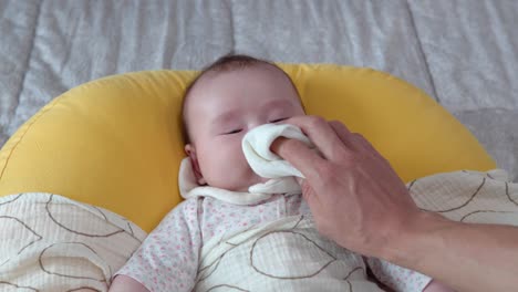 Parent's-Hands-wipe-the-mouth-of-infant-Baby-Lying-on-bed---close-up