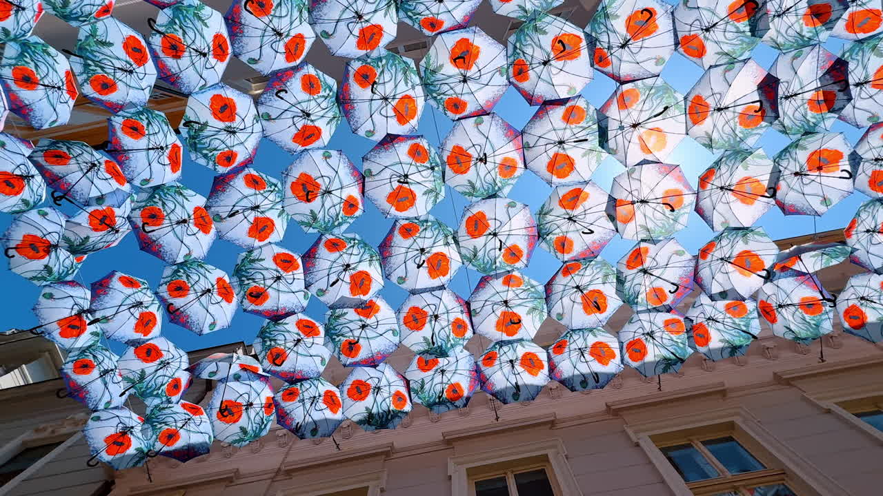 Bratislava, Slovakia, 2 June 2025: Rows of numerous umbrellas with poppy flowers hanging among the buildings in the narrow street. Low angle view at the beautiful decoration and sun protection in Bratislava, Slovakia
