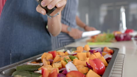 pareja diversa preparando verduras frescas y condimentos en la cocina, cámara lenta
