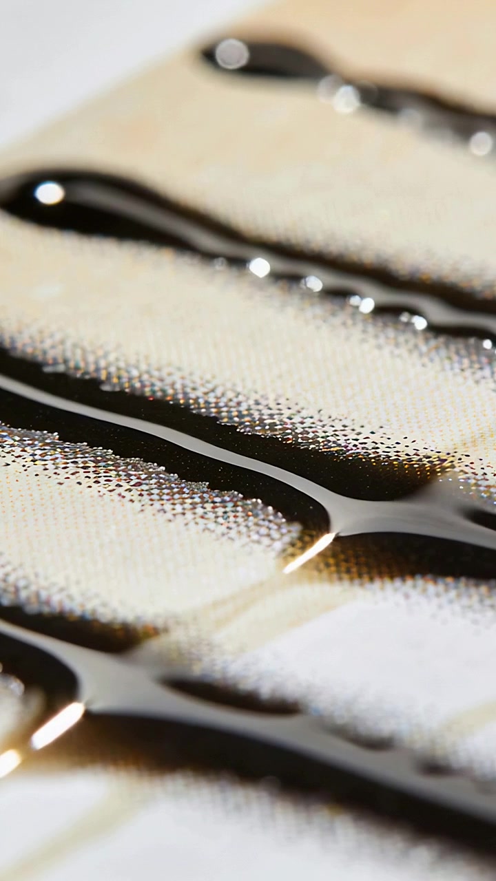 Vertical video: Forming dark syrup ribbons advancing on woven cloth, pulled by surface tension
