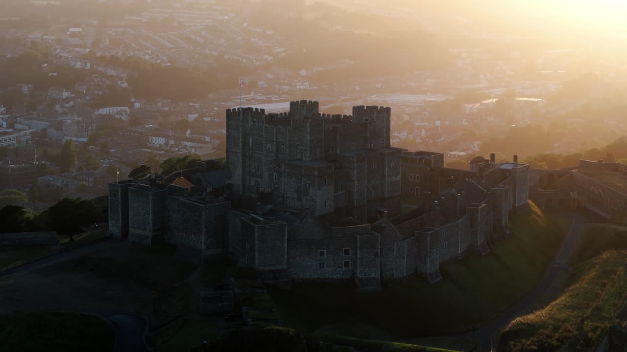 Slow drone orbit around Dover Castle reveals stone walls and surrounding green terrain, medium establishing