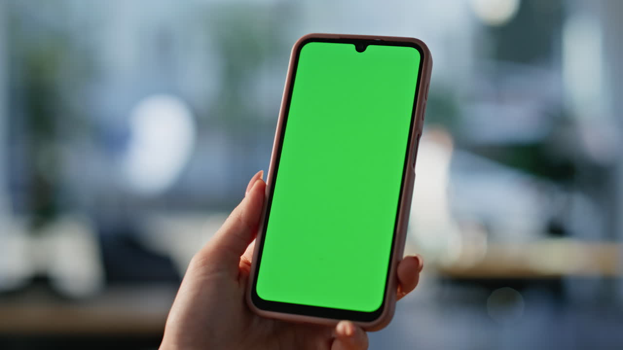 Primo piano di una mano curata che tocca lo schermo verde di uno smartphone in ufficio