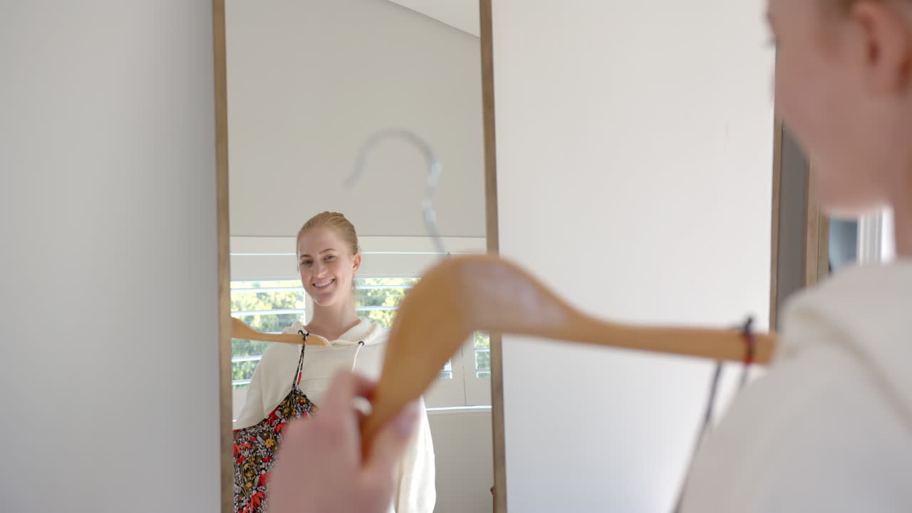 Donna sorridente che tiene un vestito su una gruccia mentre si guarda allo specchio a casa.