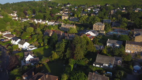 low establishing drone shot over houses rising up to reveal cow and calf rocks in ilkley spa town west yorkshire uk at golden hour