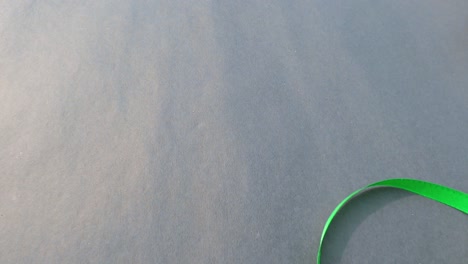 cerrar parte de la mano rodando rollo verde oscuro cinta de satén en fondo gris aislado. organizar y colocar un objeto en la mesa. concepto de arreglo de negocios.