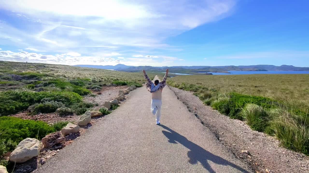 Uomo che corre e festeggia su una strada costiera panoramica verso l'oceano a Minorca, Spagna