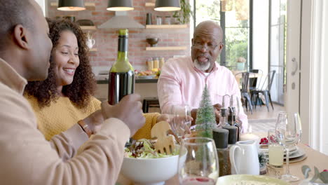 Happy-african-american-husband-pouring-wine-for-wife-and-senior-father-at-christmas-dinner-table