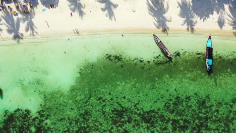 Long-tail-boats-anchoring-on-white-sandy-shore-of-tropical-island-with-exotic-beach-washed-by-turquoise-lagoon-in-Philippines