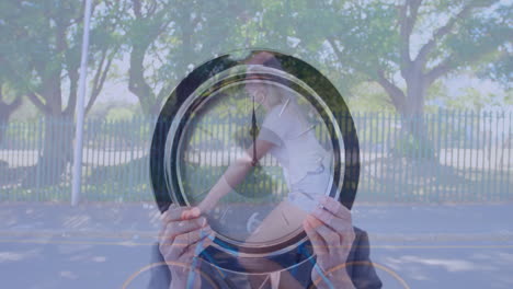 holding clock over face, person standing near trees and fence outdoors