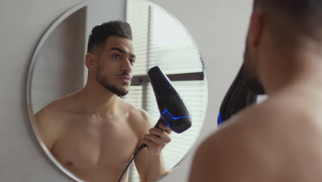 man drying hair in front of bathroom mirror