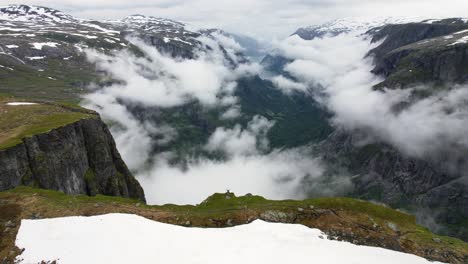 drone dando vueltas alrededor de un excursionista parado al borde de un acantilado empinado con vistas a las nubes que se forman en el valle de simadalen
