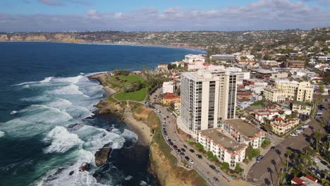 Panorámica-Aérea-Alrededor-De-Un-Edificio-De-Apartamentos-De-Gran-Altura-Junto-A-La-Costa-Con-Pequeñas-Olas-Rodando-En-La-Orilla-Con-Casas-De-Playa-En-El-Fondo