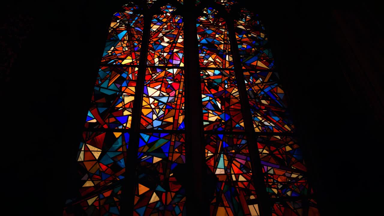 Sunlight shifting through arched stained glass window inside church, illuminating colored hues