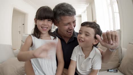 happy dad and two cute kids smiling and waving hello at webcam