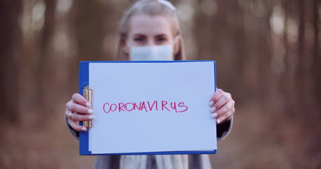 mujer con máscara protectora con inscripción de coronavirus en las manos en el bosque