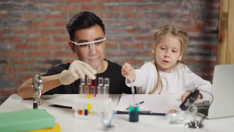 asian teacher supports girl dropping reagent into beaker