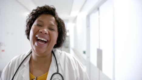 portrait of happy african american female doctor in hospital corridor with copy space, slow motion