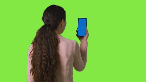 studio rear view of woman holding blue screen mobile phone against green screen