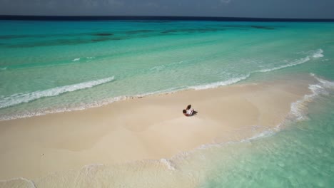 stunning aerial view woman in white walk and lying on sandbar, waves crash on white sand foam