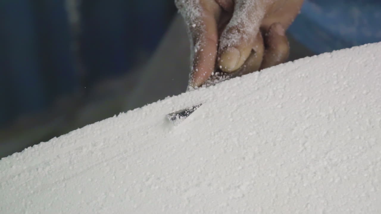 Cutting through foam board to build DIY surfboard in workshop, close up hands