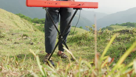 close-up-shot-of-legs-of-a-man-playing-the-piano-outside-with-grass-in-the-foreground