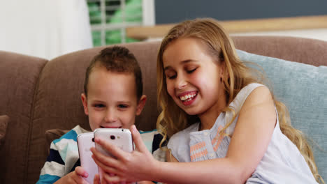 Lächelnder-Junge-Und-Mädchen,-Die-Auf-Dem-Sofa-Sitzen-Und-Ihr-Mobiltelefon-Benutzen