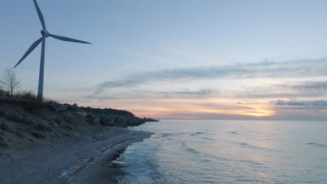 aerial view of abandoned seaside fortification buildings at karosta northern forts on the beach of baltic sea in liepaja, sunset, golden hour, wind turbine, wide drone shot moving forward low