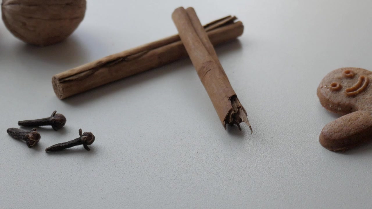 Biscotti di pan di zenzero con bastoncini di cannella su sfondo bianco evocano calde atmosfere natalizie.