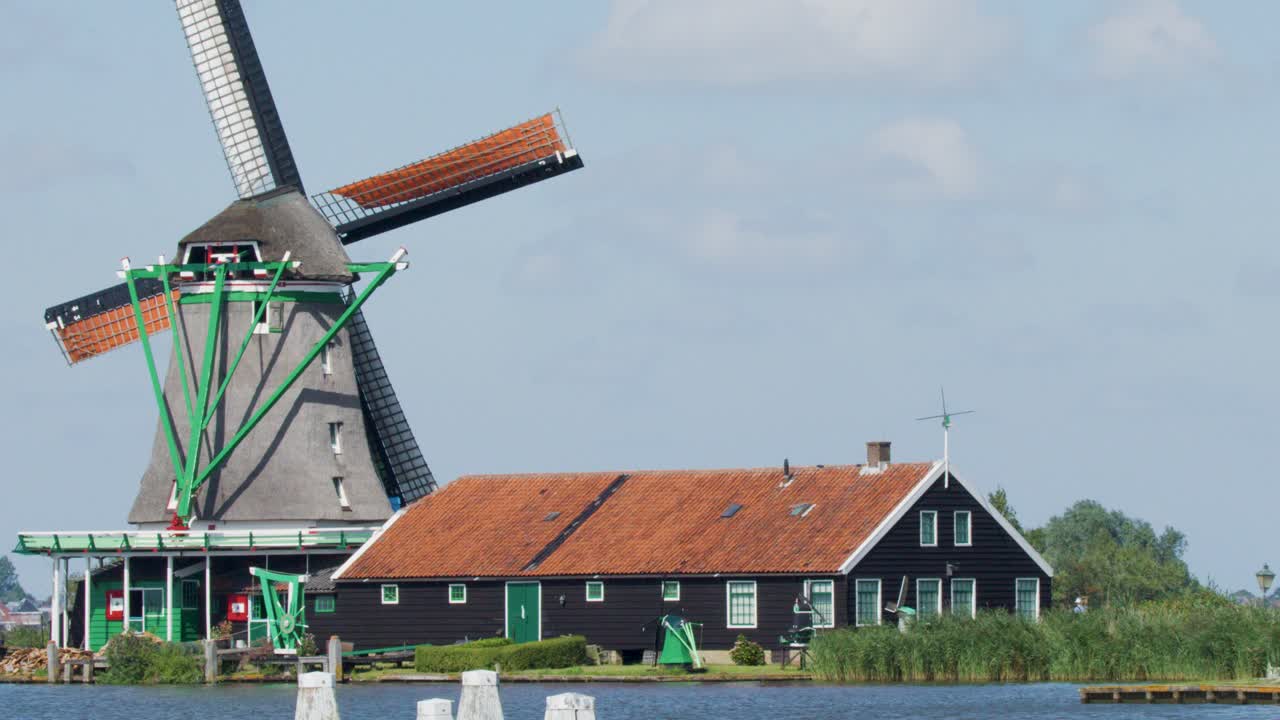 Classic Dutch windmill spinning by a river with traditional houses under clear daylight, static shot