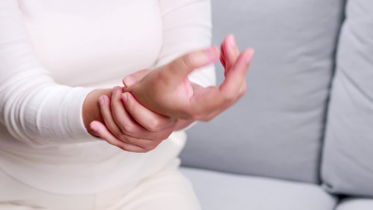 Donna seduta sul divano che si massaggia e stringe il polso per rilassarsi e alleviare il dolore