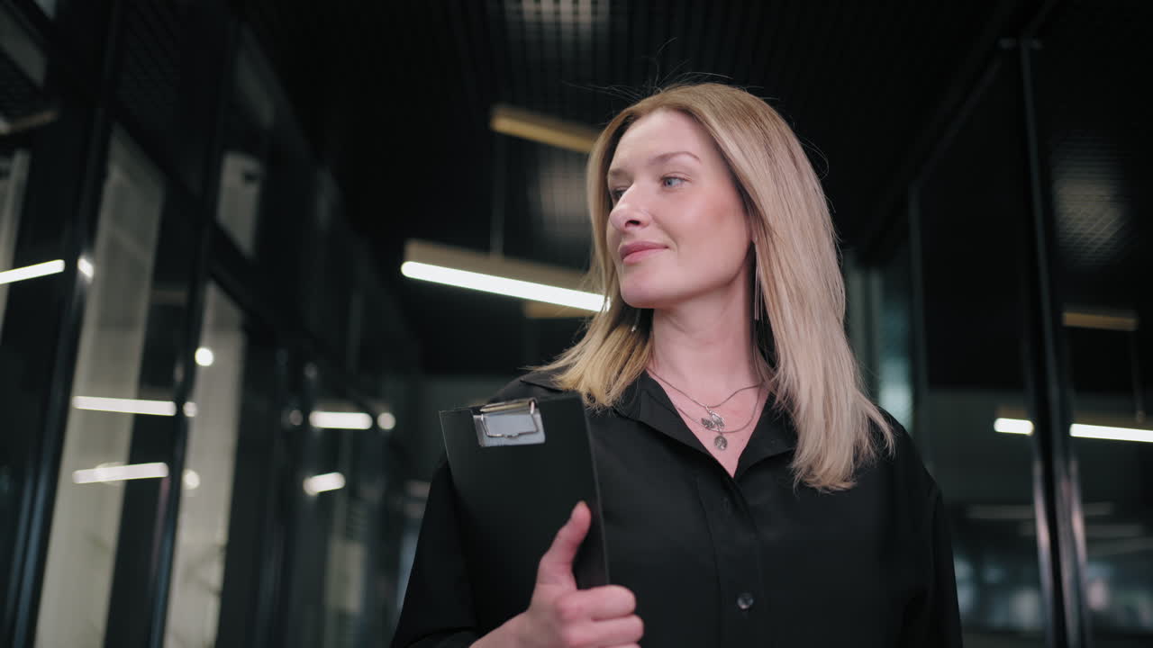 una mujer hermosa camina con documentos a lo largo del pasillo de la oficina sonriendo y mirando positivamente hacia adelante. buen día de trabajo grandes noticias