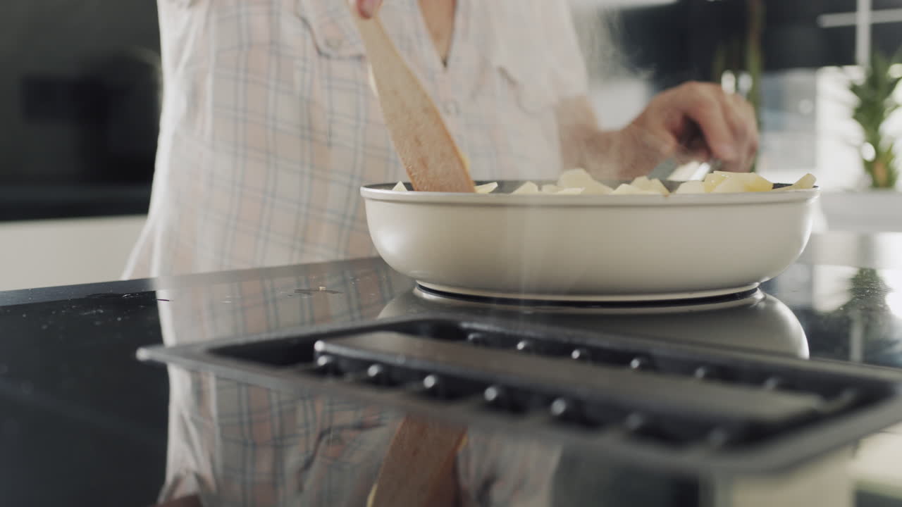 Senior woman fries potatoes on an induction electric stove with a built-in extractor fan