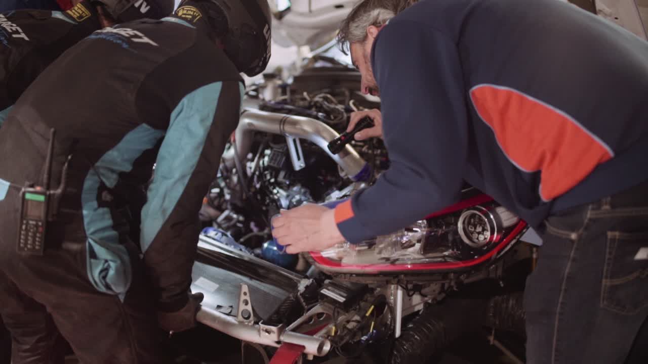 Mechanics and engineer racing team in Box Garage paddock working under time pressure to fix the engine of a race car at night at the ADAC Nurburgring twentyfour hour race.