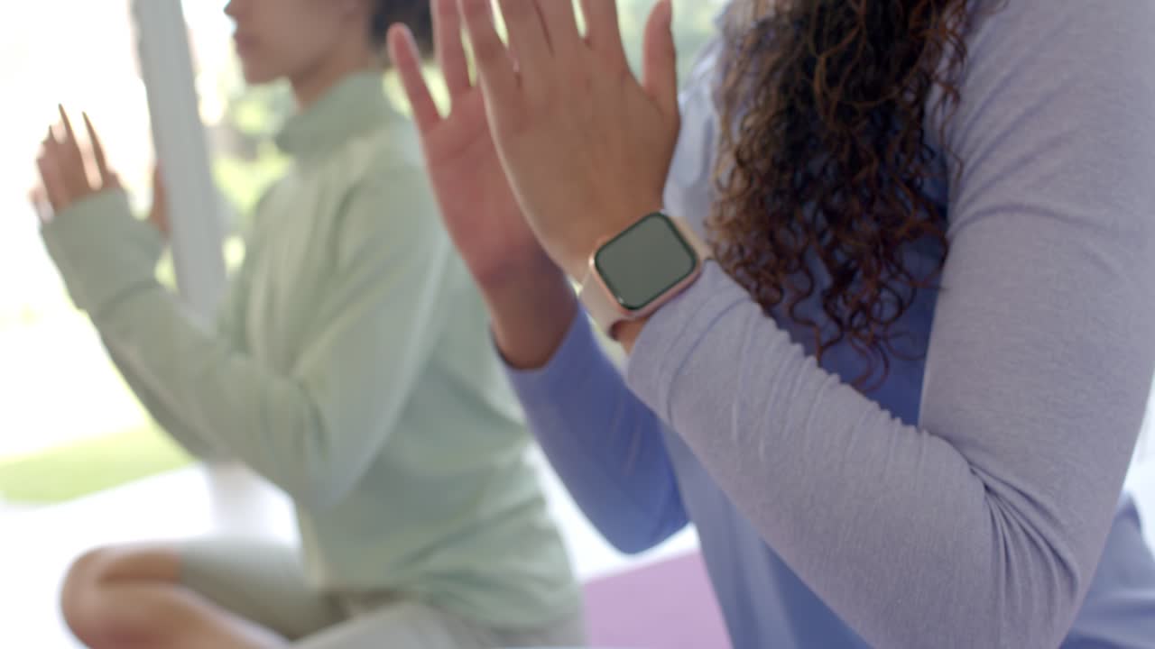 Two adult African women shifting mudra into prayer on mats as camera widens, revealing smartwatch