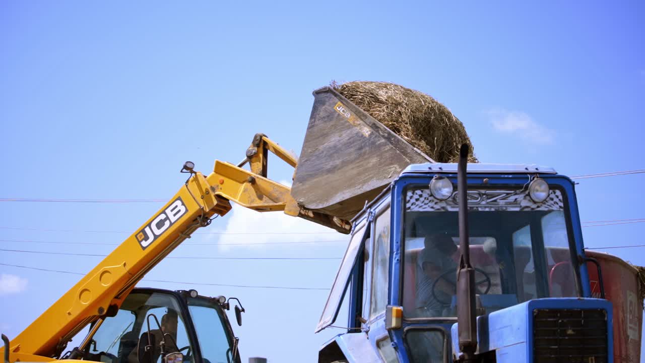 Loading hay on the trailer. Tractor loading hay on truck trailer
