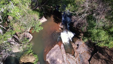 Aerial-shot-of-a-fountain-falling-down-with-dense-overgrowth-along-the-plunge-pool