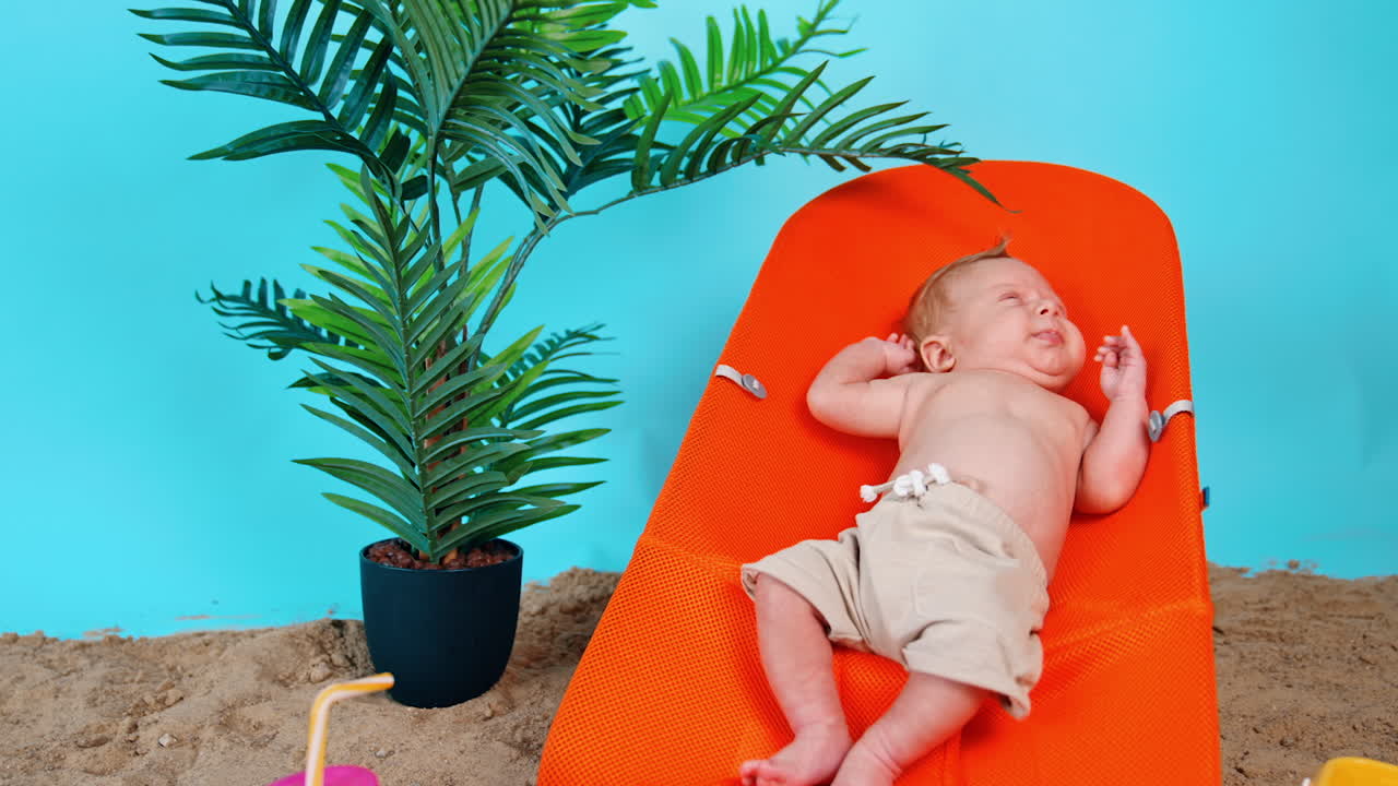 Caucasian infant moving hands and legs lying in the chair. Baby boy starts to cry. Improvised beach around.
