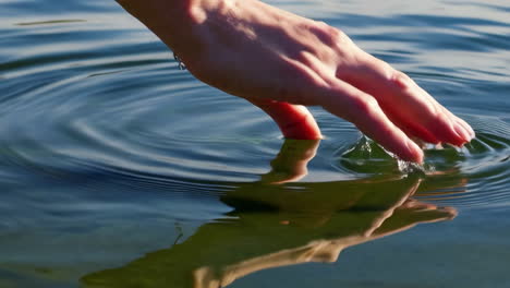 hand gently touching water surface creating ripples
