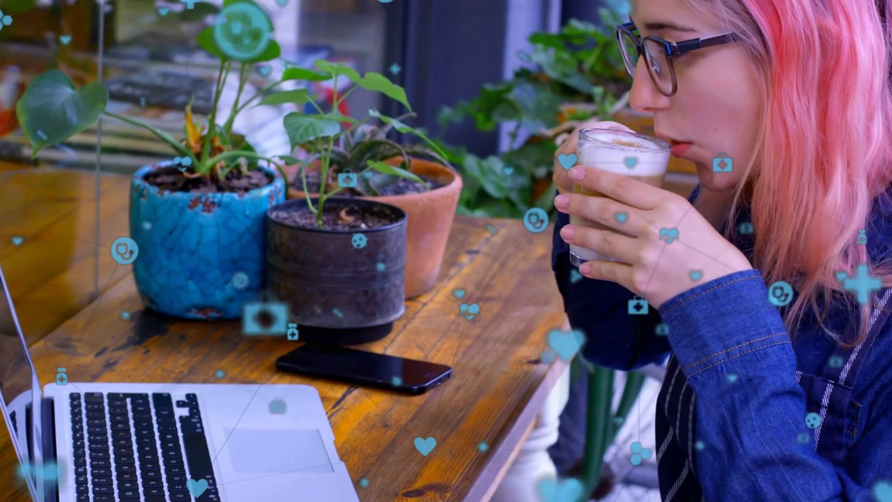 Studentessa che digita sul laptop, con icone fluttuanti che appaiono, prende un latte, lo sorseggia e riprende le attività di marketing.
