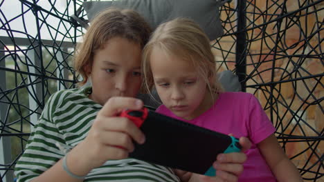 siblings playing video games on a swing chair on the balcony