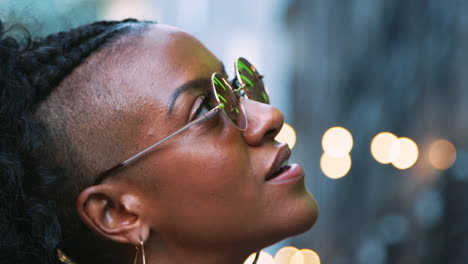 jovem negra à moda usando óculos de sol olhando para cima, tiro na cabeça, luzes bokeh no fundo